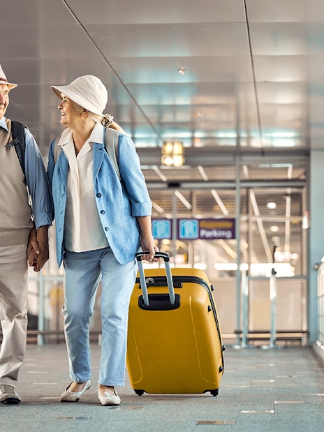 Senior couple with luggage leaving Heathrow Airport terminal.