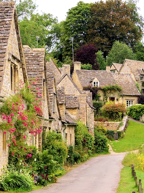 Arlington Row cottages in Bibury, Cotswolds village, with lush greenery and a serene pathway.
