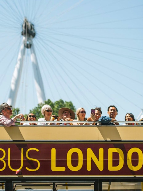 Big Bus tour in London passing the London Eye with Thames River cruise in view.