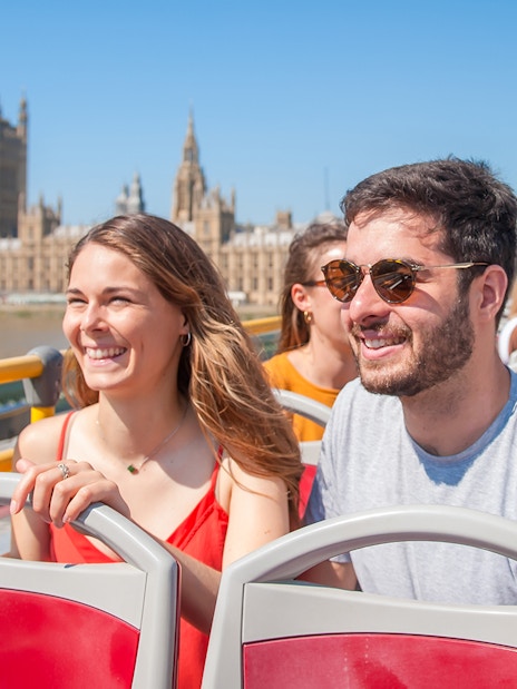Tourists on a Hop-on Hop-off bus in London with London Eye and River Thames in view.