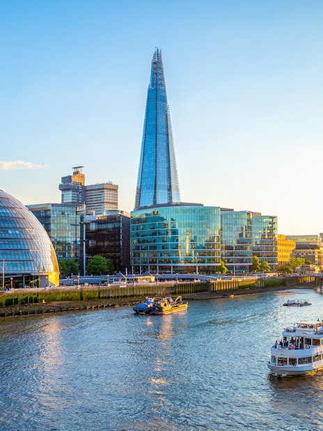Thames River Cruise boat passing under London Bridge with city skyline in the background.