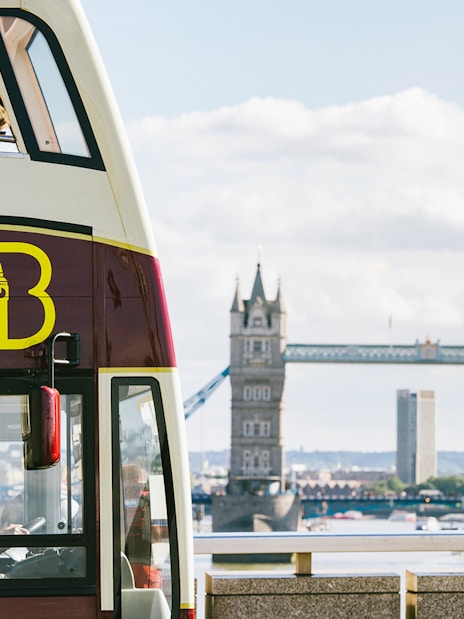 Big Bus tour passing near London Tower Bridge with view of Thames River.