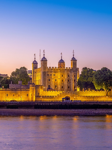 Tower of London illuminated at dusk with a view of the River Thames in London, England.