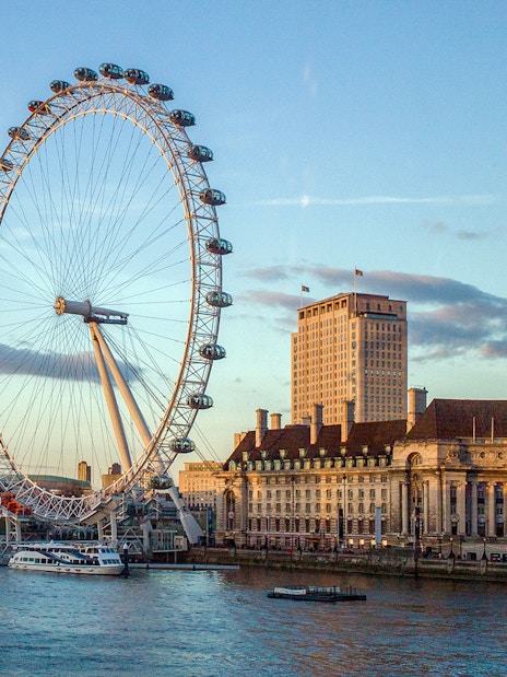 Thames River cruise boat passing under London Bridge with city skyline.